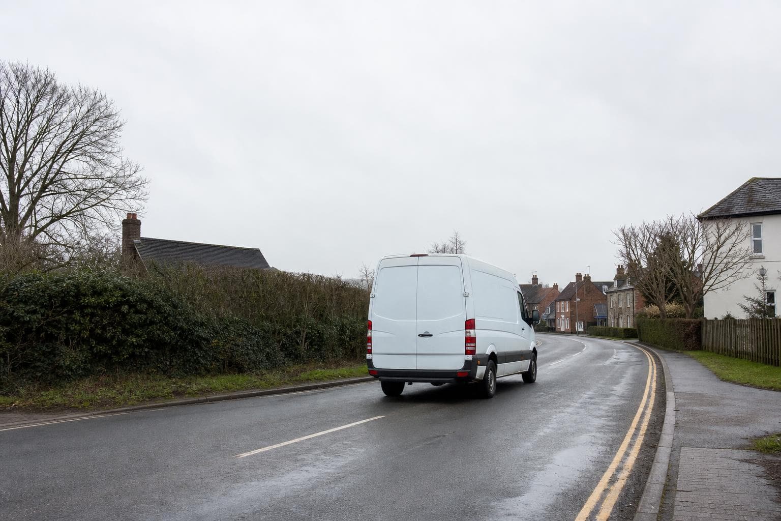Plain courier van travelling along a quiet country-edge road near Ongar on a wet day.